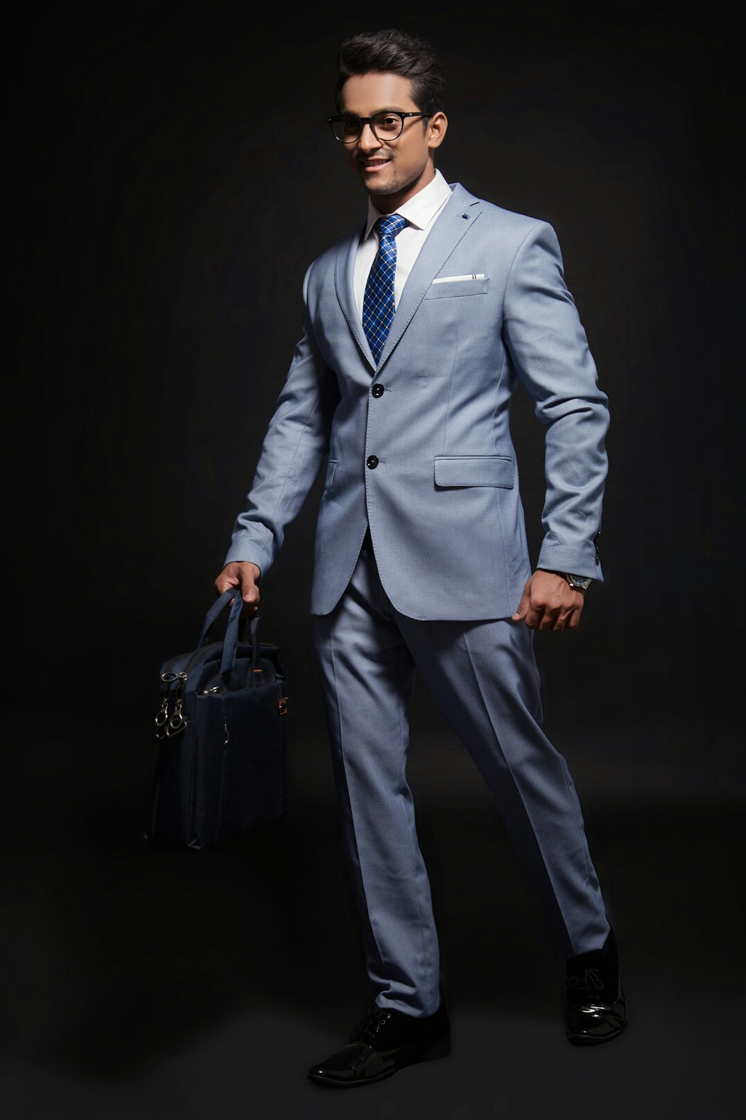 Studio portrait of a man in a light blue suit with glasses